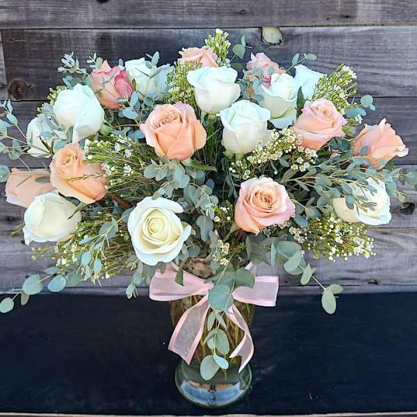 Bouquet of white and peach roses in a glass vase with a pink ribbon