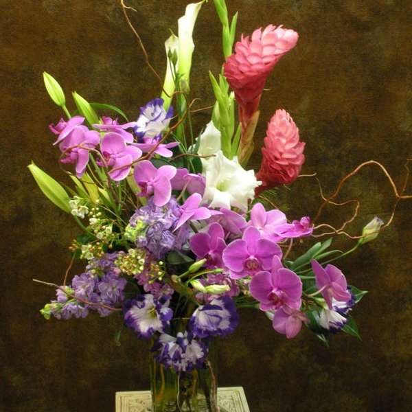 Tall mixed bouquet with pink orchids, white calla lilies, and purple blooms in a glass vase