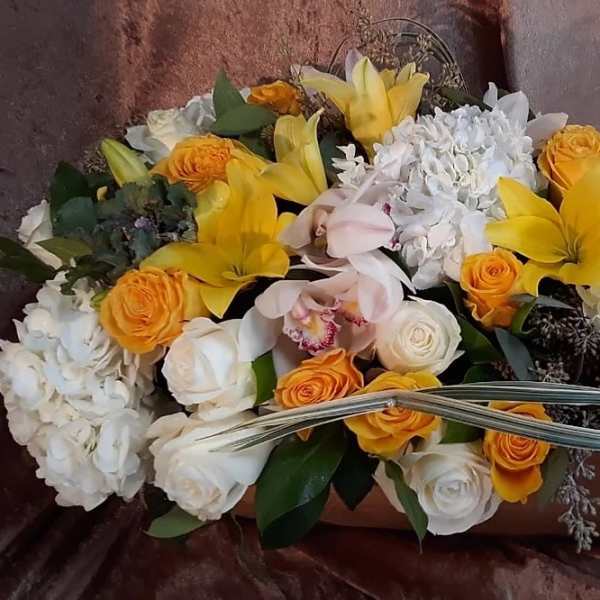 Yellow lilies and orange roses arranged with white blooms in a low container