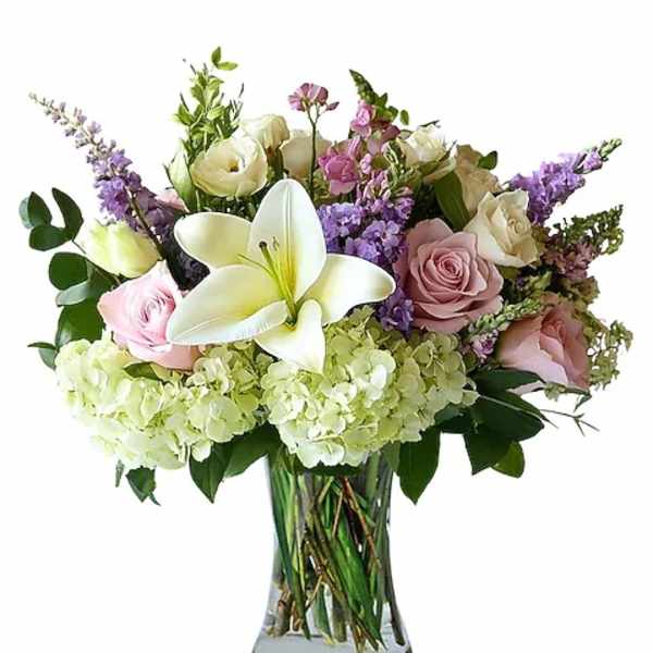 Bouquet of white lilies, roses, and purple flowers in a glass vase