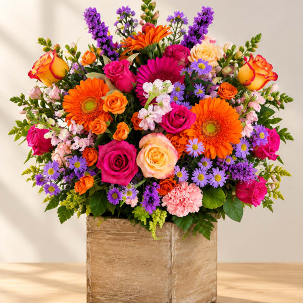 Bright mixed bouquet in a square wooden vase with pink, orange, purple, and yellow blooms