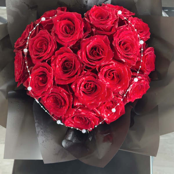 Heart-shaped bouquet of red roses wrapped in black paper with pearl accents
