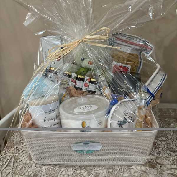 Gift basket with candles, snacks, and a teddy bear wrapped in clear cellophane