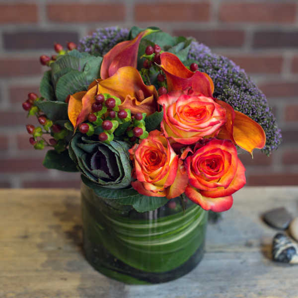 Orange roses and calla lilies in a green glass vase