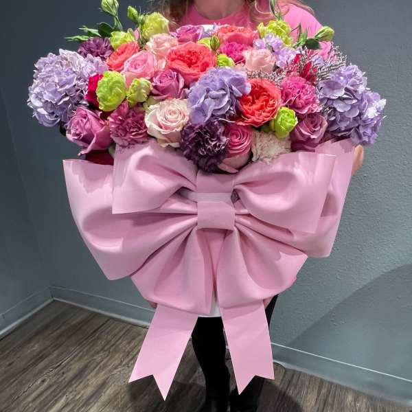 Large bouquet of pink, purple, and coral flowers with a pink ribbon wrap