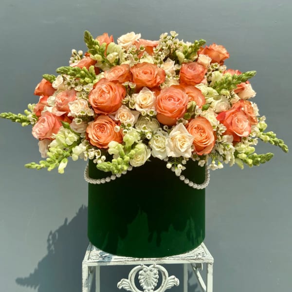 Peach and white roses arranged in a green velvet box with pearl trim
