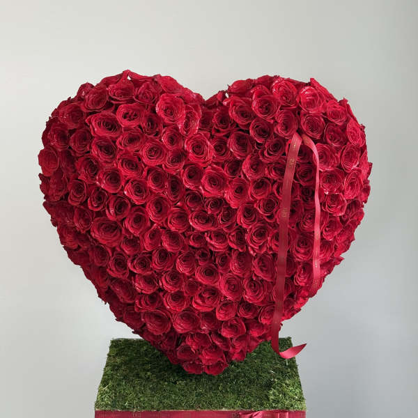 Heart-shaped arrangement of red roses on a moss-covered base with a ribbon
