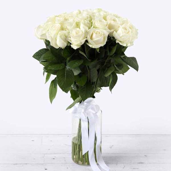 Tall arrangement of white roses in a clear glass vase with a white ribbon bow.
