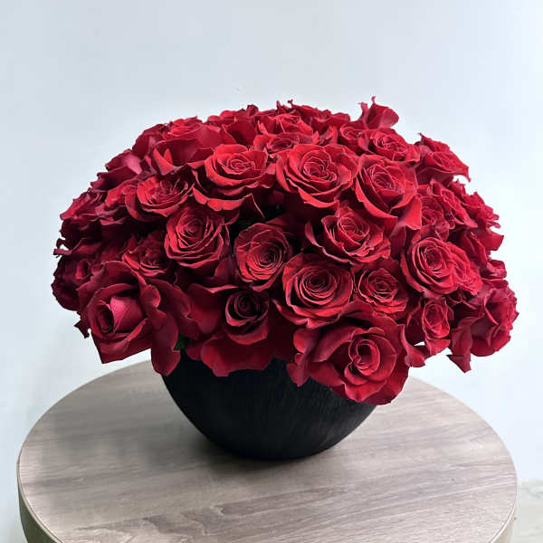 Low black bowl filled with densely packed red roses on a wooden table