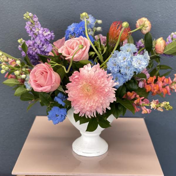 Mixed bouquet of pink roses, blue hydrangeas, and purple blooms in a white vase