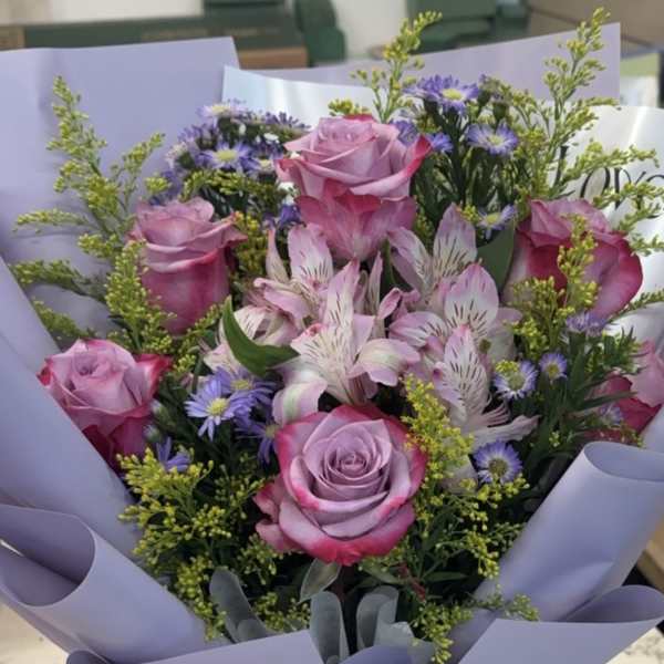 Bouquet of pink roses and purple flowers wrapped in lavender paper