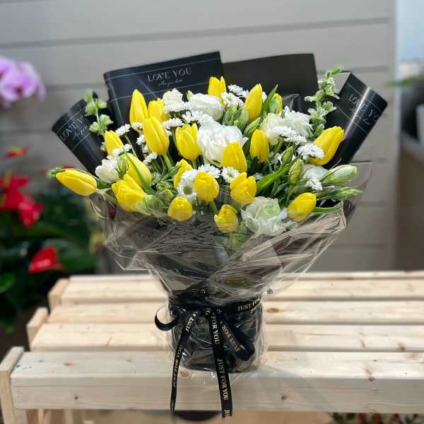 Bouquet of yellow tulips and white flowers wrapped in black paper