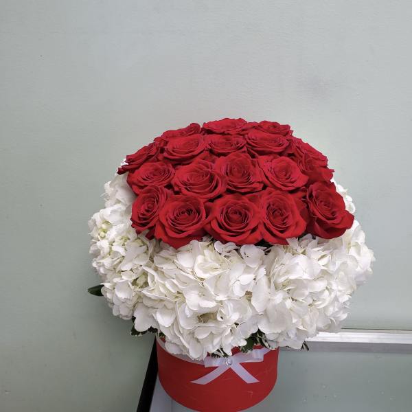 Red roses arranged over white hydrangeas in a red hat box