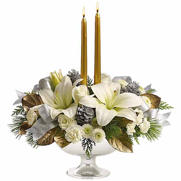 White lilies and roses arranged in a glass compote with two gold taper candles