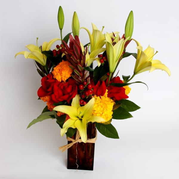 Bouquet of yellow lilies and red roses in a brown glass vase