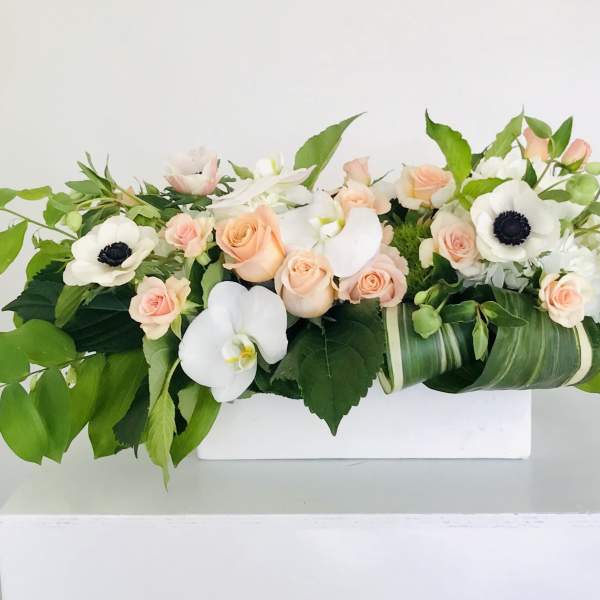 Low floral arrangement with peach roses and white anemones on a white stand