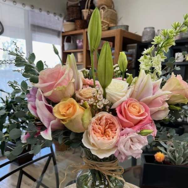 Mixed bouquet of pink roses, lilies, and white blooms in a glass vase