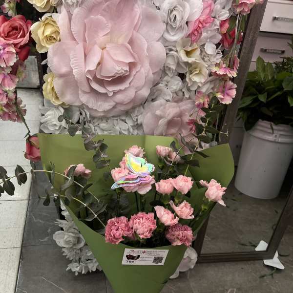 Pink carnations in green wrap with a pink ribbon, in front of a floral display