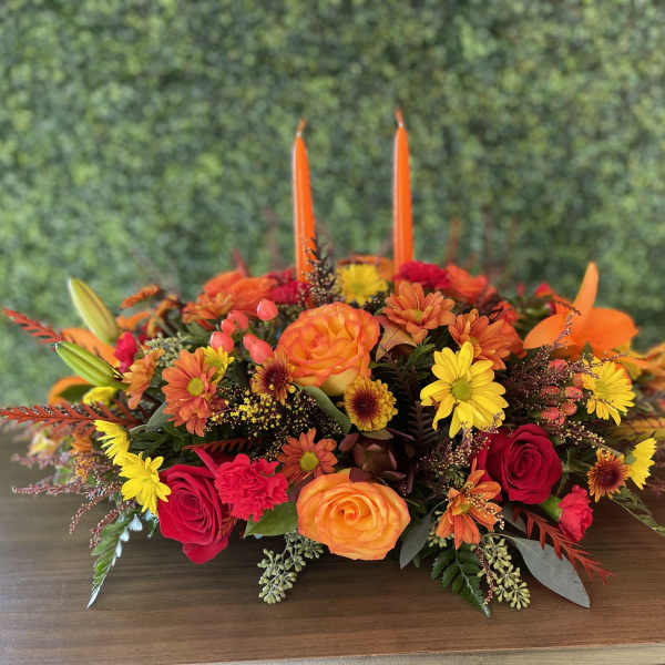 Low floral centerpiece with orange, red, and yellow blooms and two tall orange candles