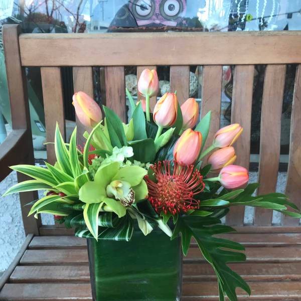 Pink tulips and tropical flowers arranged in a square glass vase