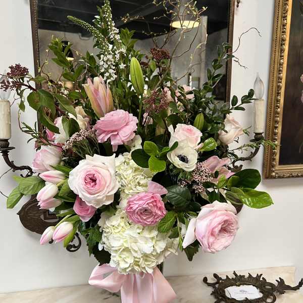 Pink and white floral arrangement in a glass vase with a pink ribbon