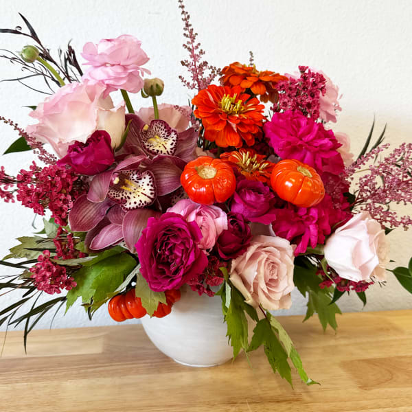 Bright mixed bouquet in a white vase with pink, orange, and magenta blooms