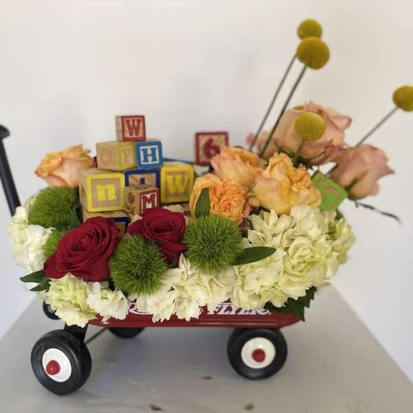Flower arrangement in a red wagon with roses, hydrangeas, and alphabet blocks