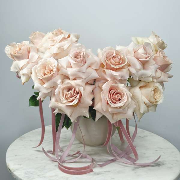 Blush pink roses arranged in a white vase with pink ribbons