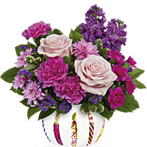 Pink and purple flower arrangement in a white vase with candle designs