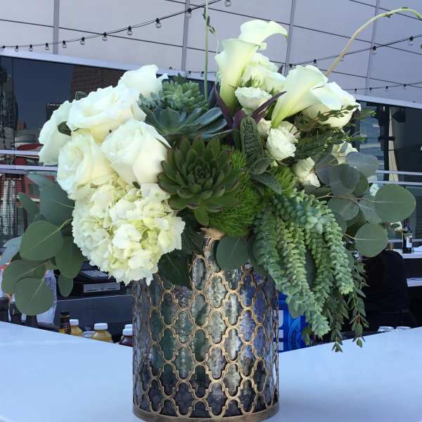 White roses and calla lilies arranged with succulents in a patterned metal vase