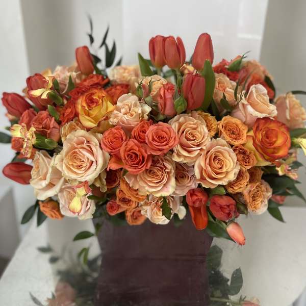 Bouquet of peach and orange roses with red tulips in a dark vase