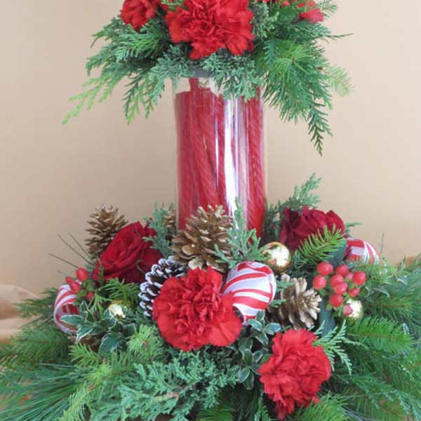 Holiday floral arrangement with red carnations and pinecones in a tall glass vase