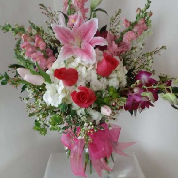 Pink and white mixed bouquet in a clear glass vase with a pink ribbon