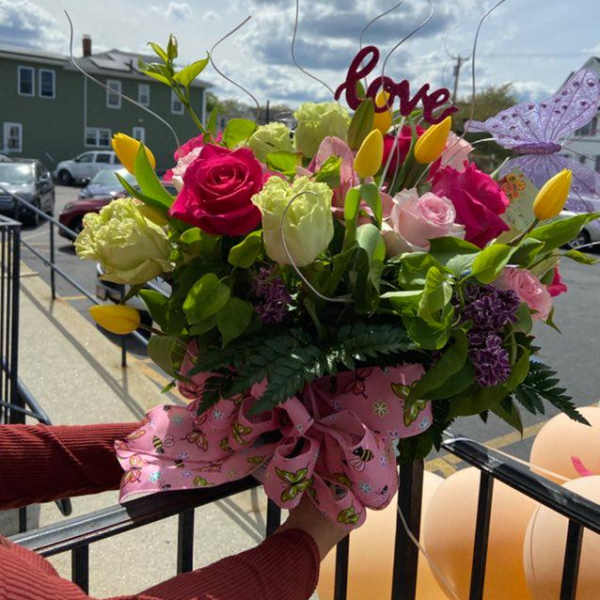 Bouquet of pink and yellow flowers with a pink ribbon and "love" topper
