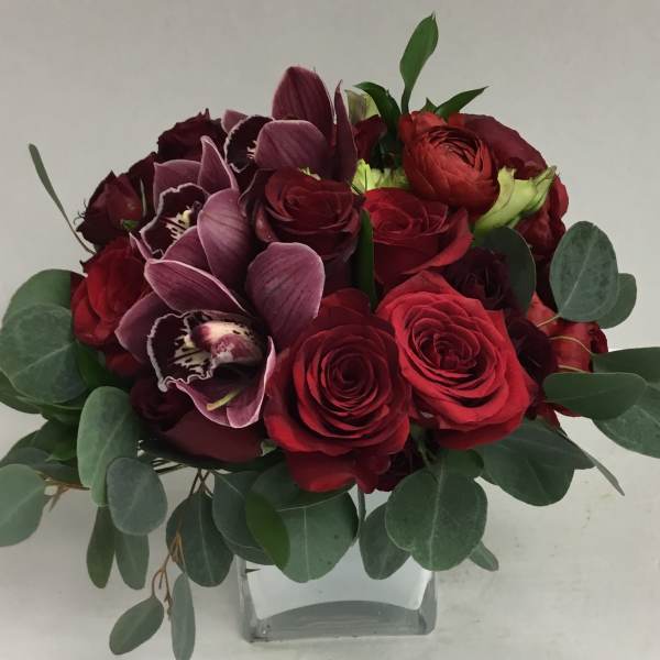 Red roses and purple orchids in a clear glass vase with eucalyptus