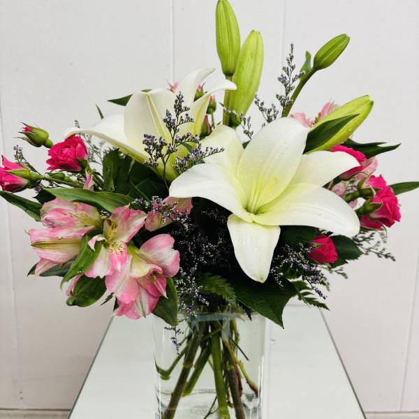 White lilies and pink flowers arranged in a clear glass vase
