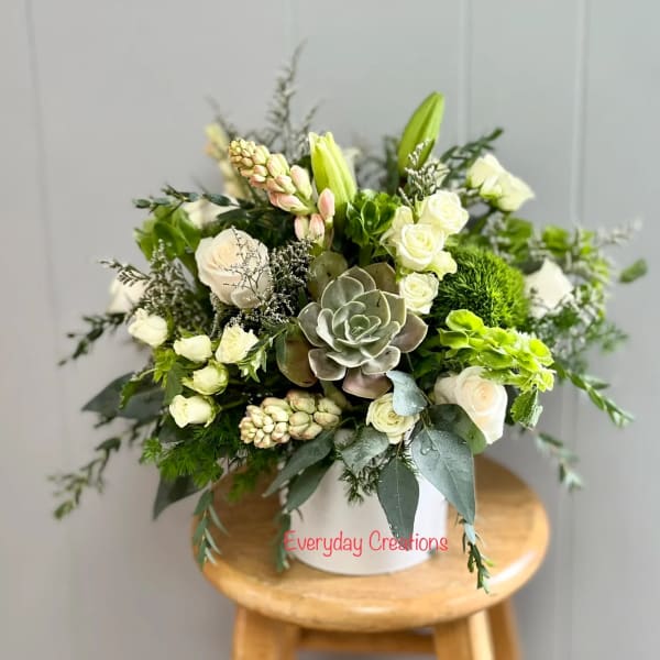 White and green floral arrangement in a white container with a succulent center
