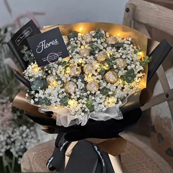 Bouquet of white baby's breath with small gold-wrapped chocolates and warm lights