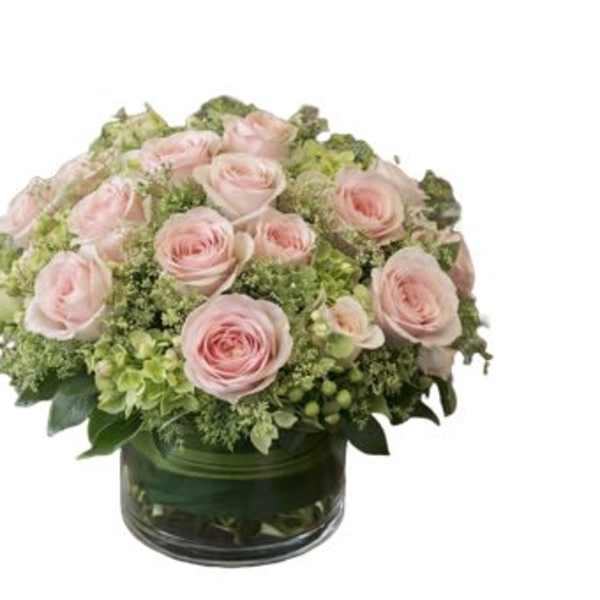 Pink roses arranged in a low glass vase with green hydrangeas