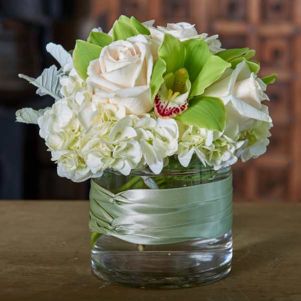 White roses and hydrangeas in a glass vase with a pale green ribbon