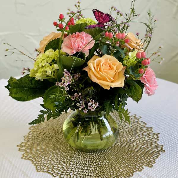 Mixed bouquet of peach roses, pink carnations, and green hydrangea in a glass vase