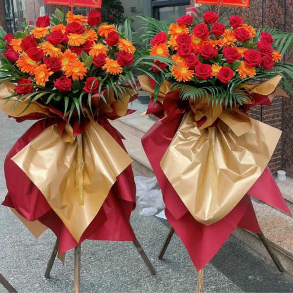 Two large bouquets of red roses and orange daisies wrapped in gold and red paper