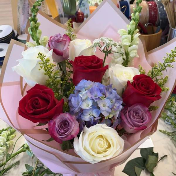 Bouquet of red, white, and lavender roses with blue hydrangea in pink wrap