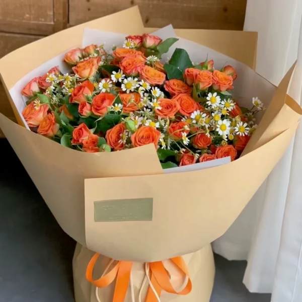 Bouquet of orange roses and white daisies wrapped in tan paper