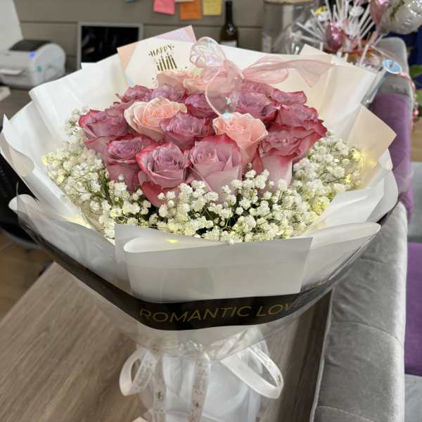 Pink roses wrapped in white paper with baby's breath and a ribbon