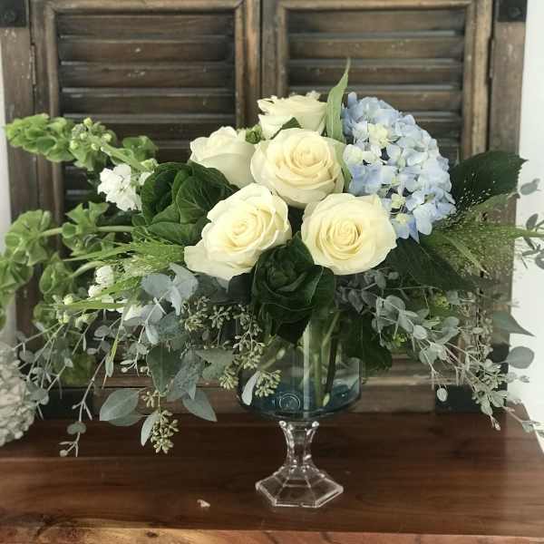 Cream roses and blue hydrangea in a glass pedestal vase