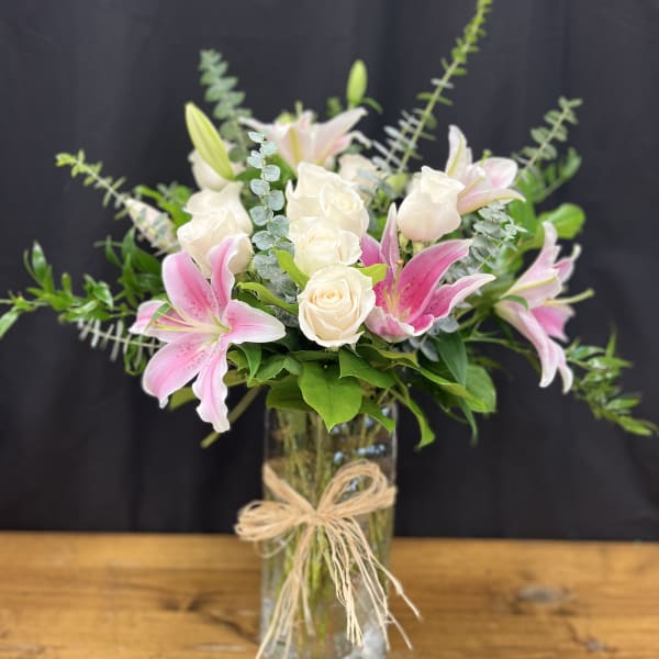 Pink lilies and white roses in a glass vase with a raffia bow