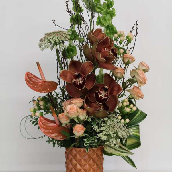 Tall arrangement with brown orchids, peach roses and tropical blooms in a textured terracotta vase