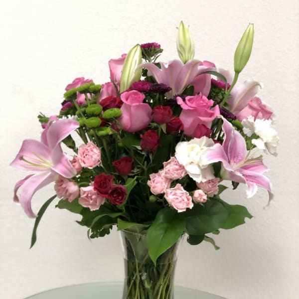 Pink lilies and roses arranged in a clear glass vase