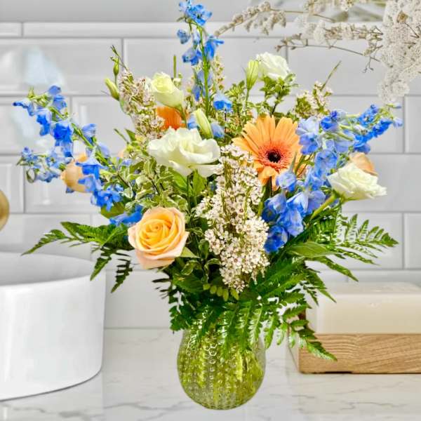 Mixed bouquet of blue, white, and peach flowers in a green glass vase